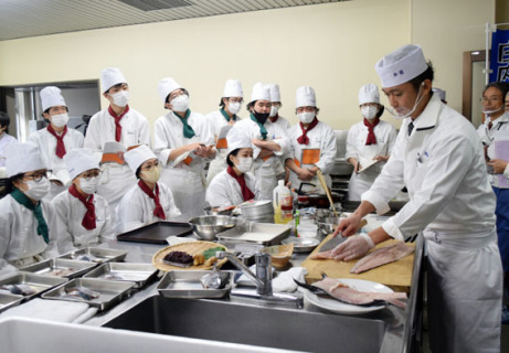 関野さん（右）らの指導でおばこサワラを使った料理を学ぶ学生たち
