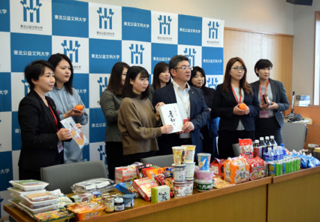 収集した食品を前に、樫木オフィス長（中央右）が鈴木代表に贈呈＝26日、公益大