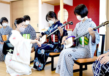 小鈴姐さん（左）から三味線、ばちの持ち方を習う参加者たち＝25日、酒田小鈴