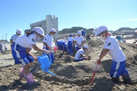 力を合わせて砂のアートの完成を目指す児童たち