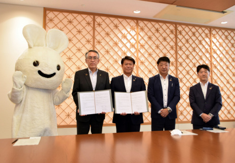 協定書を交わす丸山市長（右から4人目）と菊地執行役員（同3人目）。左は「メリーズうさちゃん」