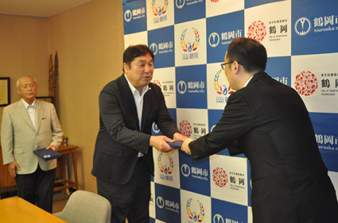 斉藤区長（中央）が皆川市長（右）から鶴岡シルクのスカーフを受け取った。左奥は芳賀さん