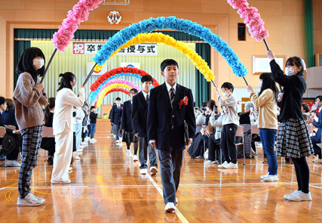 アーチをくぐって学びやを巣立つ卒業生たち＝18日午前、八幡小