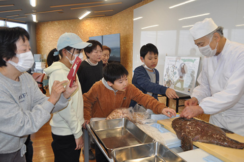 石塚さん（右）の勧めで子どもたちが恐る恐るアンコウを触ると、ヌルっとした感触に悲鳴が起こった
