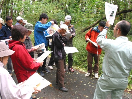荒れた森林に入り県の担当職員から状況を聞くバスツアー参加者