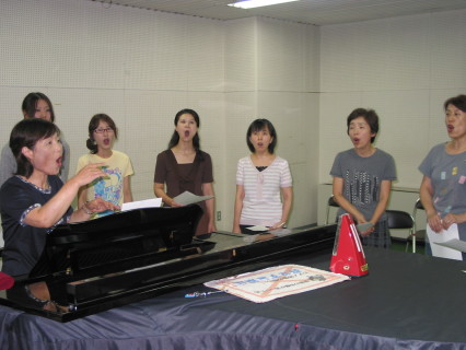 佐藤代表（左）の指導でＰＲソングを歌うＳＡＫＡＴＡローゼンコールのメンバー