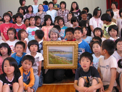 内郷小の子供たちに囲まれて笑顔の清美さん（中央）。手にしているのが寄贈した「夏の河畔」