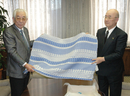 田中理事長（左）からキビソを素材に作成したタペストリーが富塚市長に手渡された