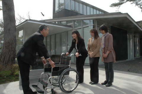 藤沢周平記念館前で佐藤会長が榎本市長に車いすを手渡した