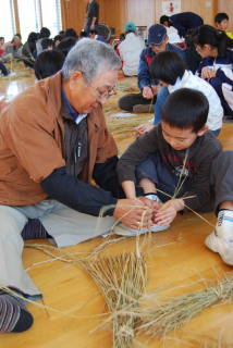 「こうやってわらを足していくんだ」。地域のお年寄りに教わりながら縄ないをする東郷小の児童たち