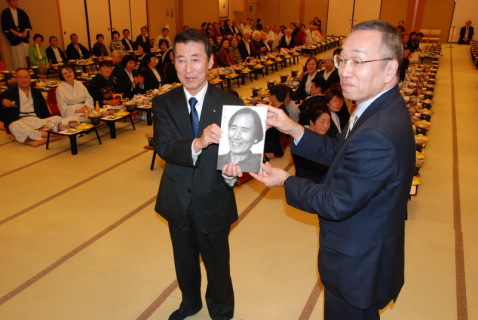 飯能信金の町田常務（左）に藤沢記念館の図録を贈る榎本市長