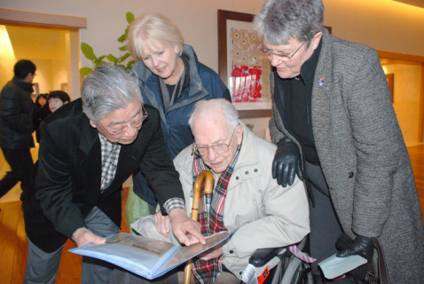 松本照太郎さん（左）から59年に来酒した際の新聞記事を見せてもらい懐かしむリチャーズさん（右から2人目）