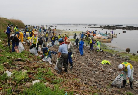 海岸に流れ着いたごみを拾い集めるボランティア。ごみは漁師の漁船（中央奥）で勝浦港に運ばれた