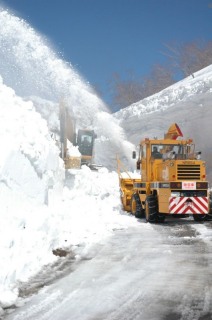 青空の下、湯殿山神社への有料道路の除雪作業が進む＝12日午後