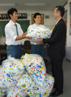 生徒会長の阿部君（中央）、前会長の高橋君（左）が、全校で集めたペットボトルのふたを引き渡した