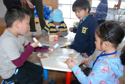牛乳パックやペットボトルで作ったスプーンと皿で非常食を食べる子供たち