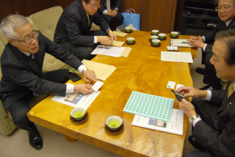 「食の都庄内」広報官とプリントされた名刺添付用シールを渋谷議長（右）に渡す佐藤支庁長（左）