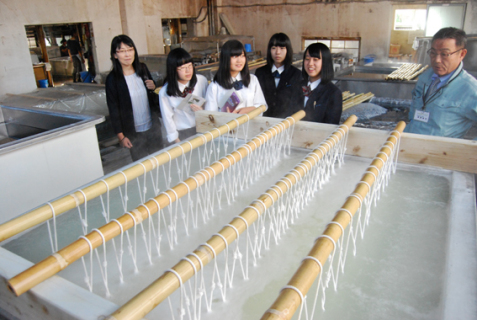精練作業の準備段階で95度のお湯に浸された織物を見学する女子生徒たち＝羽前絹練
