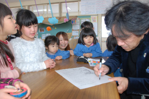 土田さん（右端）が挿絵を描く姿に、園児たちは興味津々