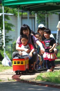 新緑の児童遊園でミニ電車に乗って楽しむ親子連れ