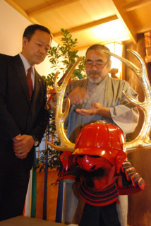 「現代版　忠次公兜・面具」を前に、解説する熱田さん（右）と、石原宮司