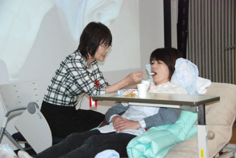 患者や要介護者の食事介助の実習で、ベッド上の姿勢確保やスプーンの使い方を紹介する小山さん（左）