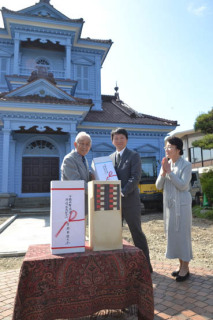 6月に一般公開される旧鶴岡警察署庁舎前で小林会長（左）が酒井副館長（中央）に陶製傘立てを手渡した