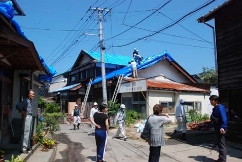 屋根瓦を撤去しブルーシートで覆う業者の作業を見守る住民たち