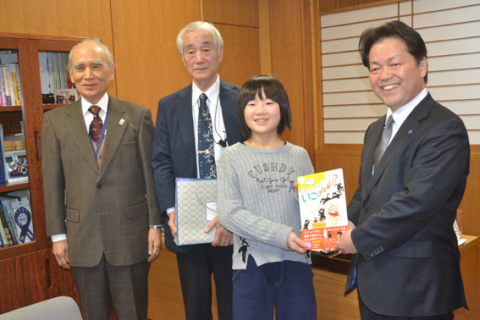 布川教育長（右）に囲碁入門書を手渡し、女流アマ選手権出場を報告した上野さん（右から2人目）