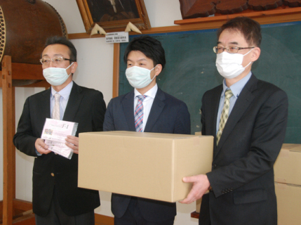 心のこもったマスクを手に左から同社斎藤悟工場長、伊藤社長、松田校長