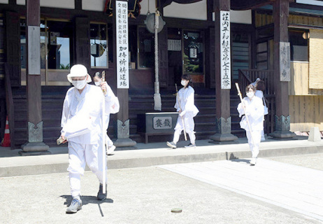白装束に身を包み即身仏が安置されている寺院などを巡る参加者たち＝16日午後、酒田市の海向寺