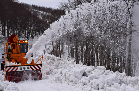 ロータリー除雪車が雪を勢いよく山間に吹き飛ばした