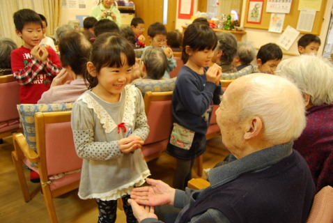 お年寄りの手を取って触れ合い遊びをする美咲保育園の年長児